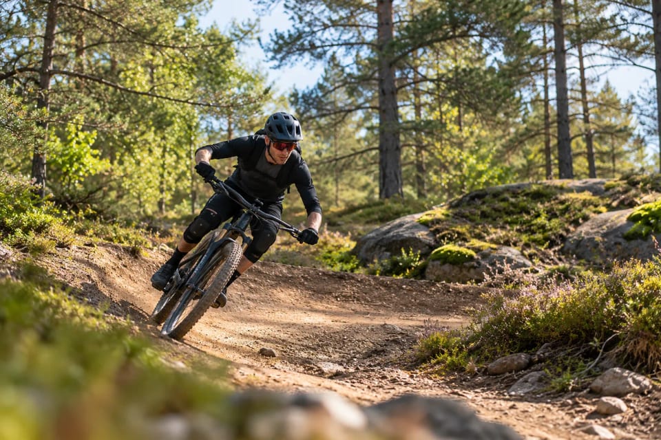 Framemaat en sweet spot: mountainbiker legt de fiets schuin in een bocht op een bospad, met het lichaam laag boven het midden van de fiets