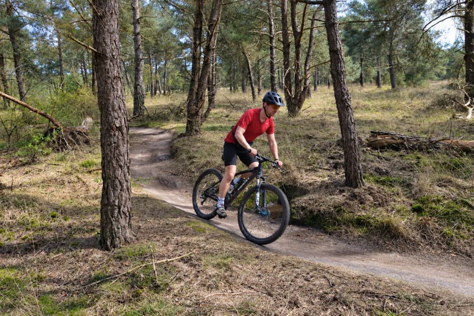 Mountainbiker in een rood shirt neemt een kombocht tussen de dennen op de MTB route Tilburg